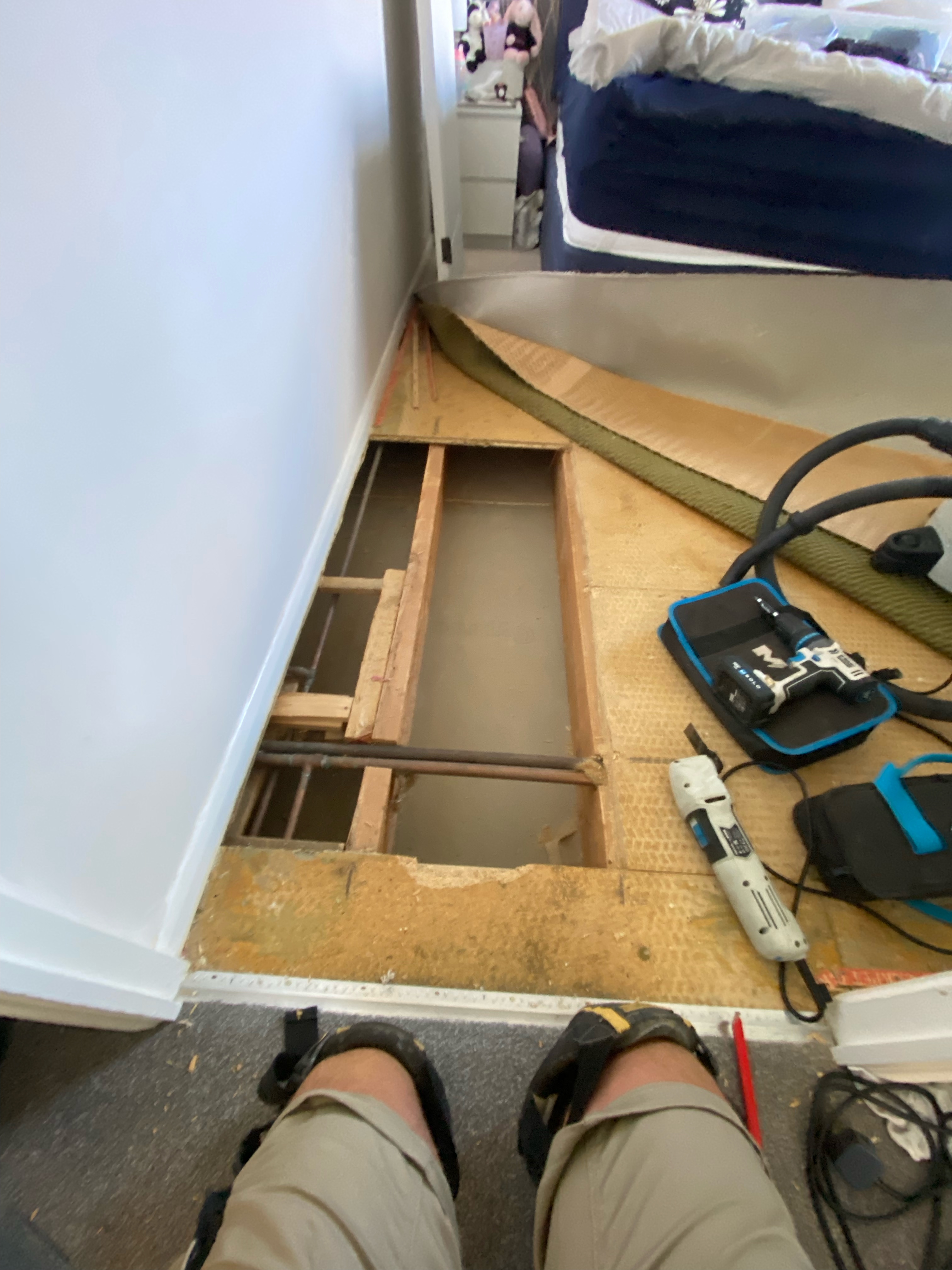 Bedroom floor opened for repair, showing exposed timber structure, pipework and tools.