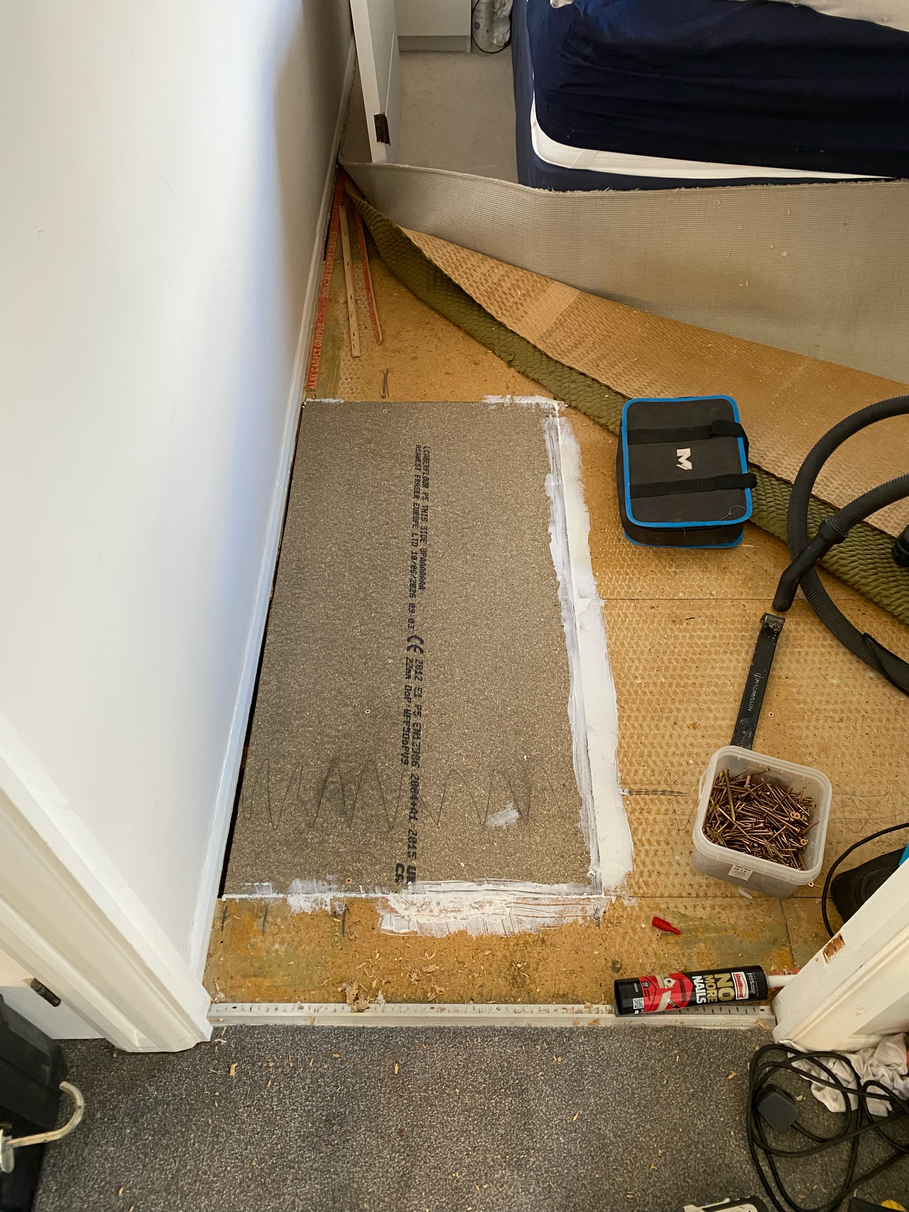 Replacement board being fitted during a bedroom floor repair, with the carpet lifted back and tools nearby.