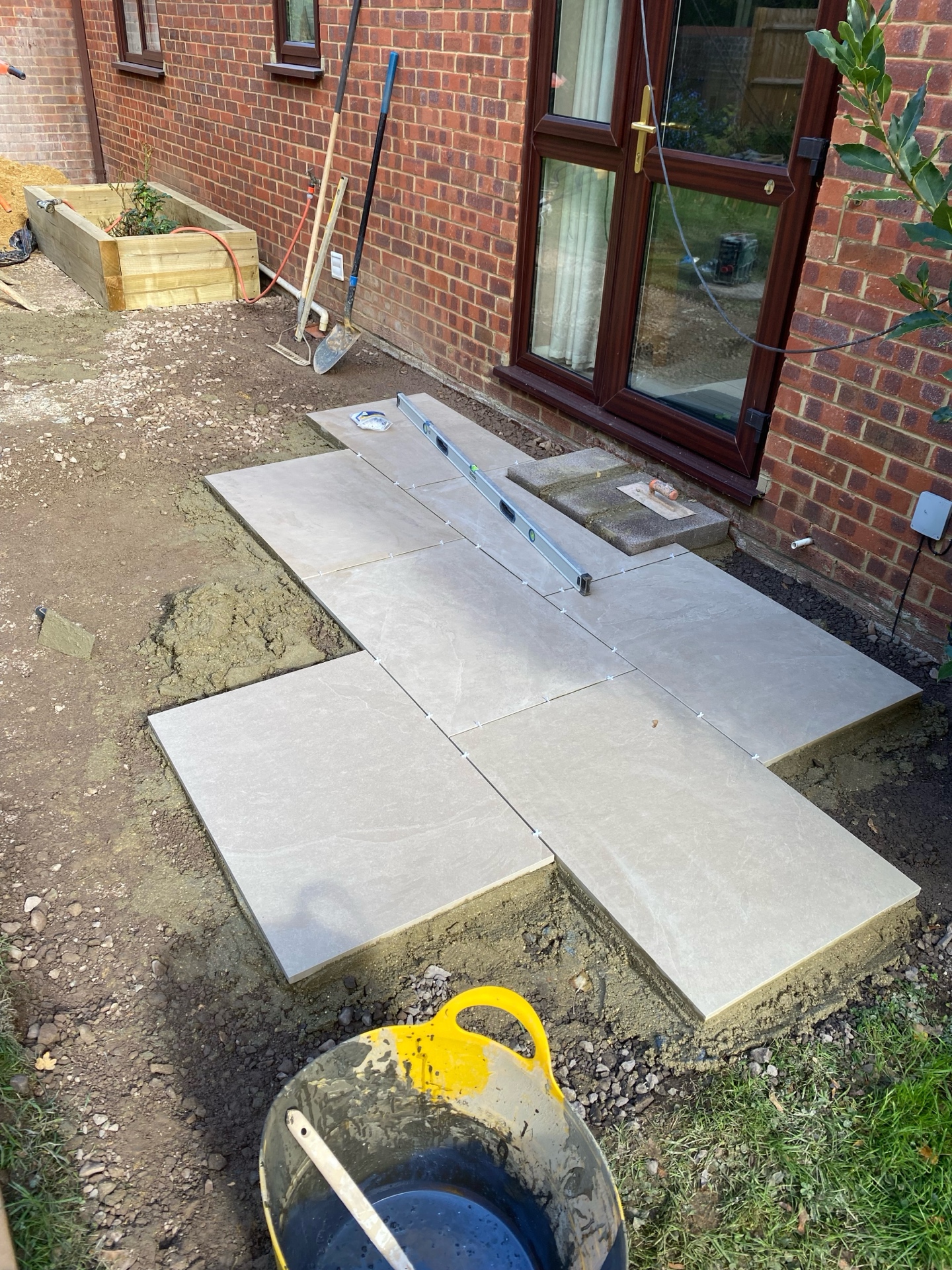 Large-format patio slabs being aligned with spacers and a spirit level during installation beside a brick house.